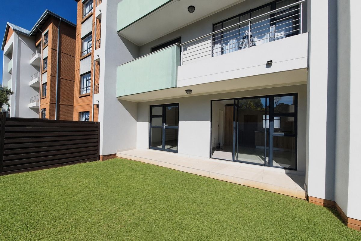 A ground floor townhouse unit featuring a private garden, tiled patio, and modern sliding glass doors leading into the living area.