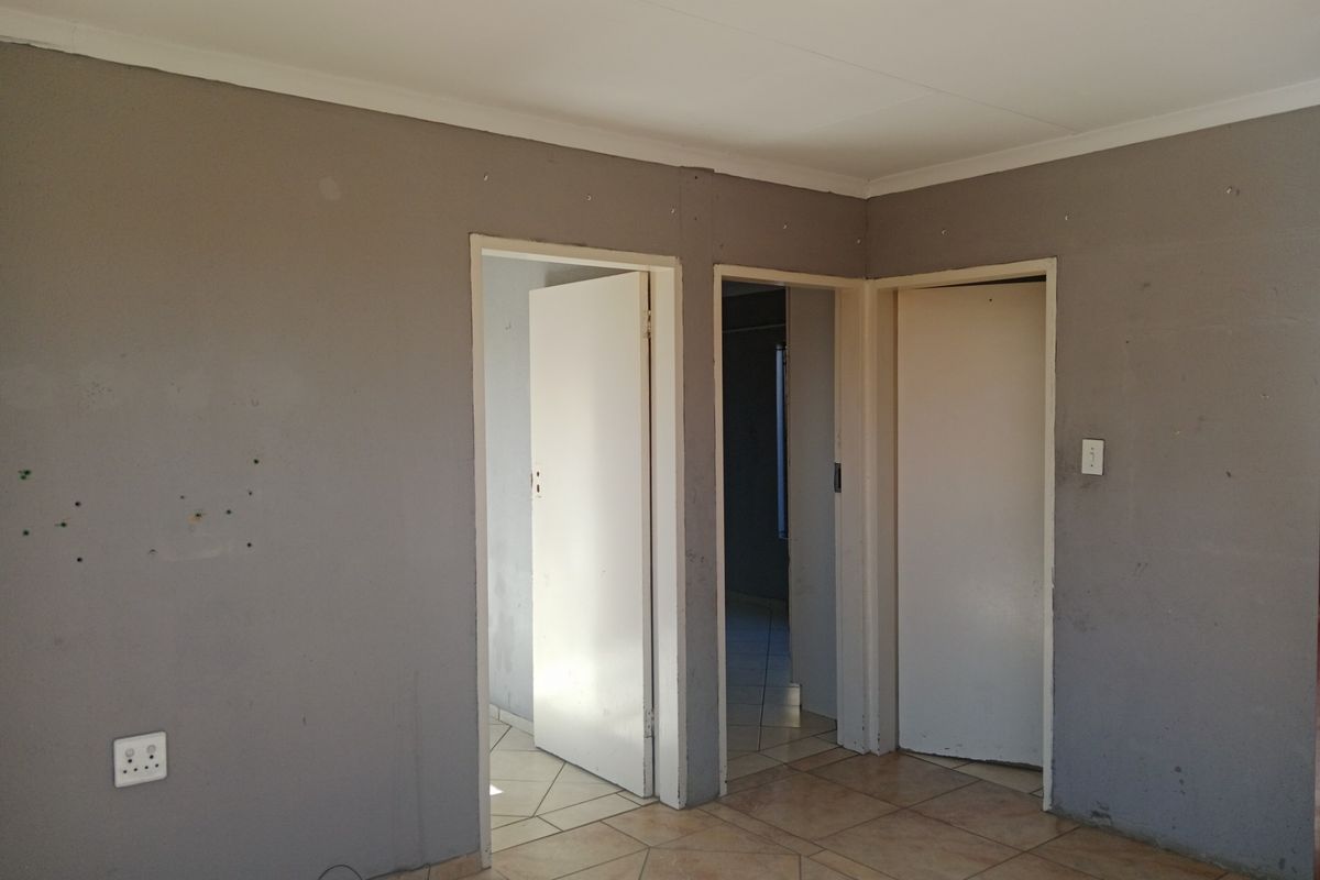 An interior view of a room featuring tiled flooring and multiple doorways leading to adjacent spaces, showing signs of wear and requiring cosmetic updates.