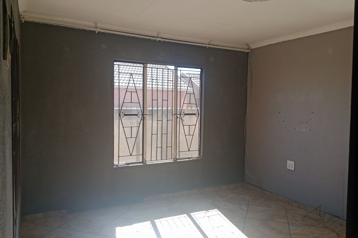 An empty bedroom featuring tiled flooring, dark grey painted walls, and a window fitted with security burglar bars.
