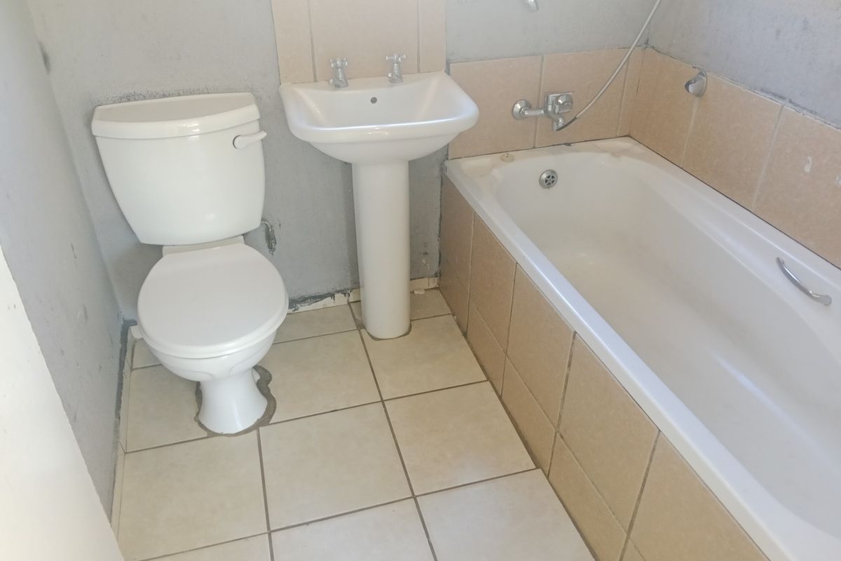 A basic bathroom featuring a standard pedestal basin, toilet, and bathtub with tiled surround, currently requiring cosmetic finishing and wall repairs.