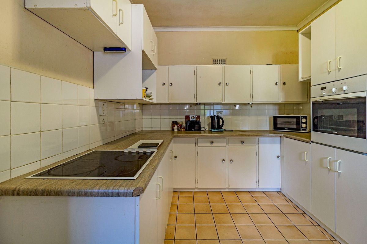 A dated kitchen featuring white cabinetry, laminate countertops, ceramic tile backsplash, and built-in oven, offering significant potential for modernization and renovation.