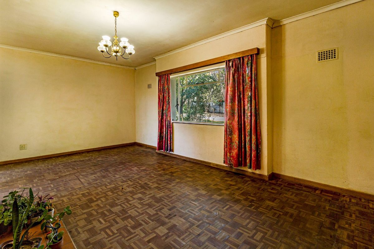 A spacious, empty living room featuring original parquet flooring, coved cornicing, and a large window, offering a blank canvas for renovation and modernization.