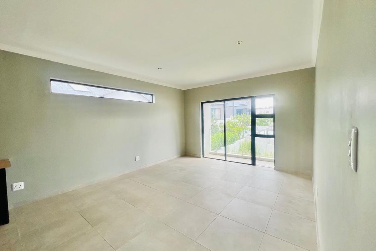 A bright, empty living room featuring large format floor tiles, recessed downlighting, and sliding glass doors leading to an outdoor area.