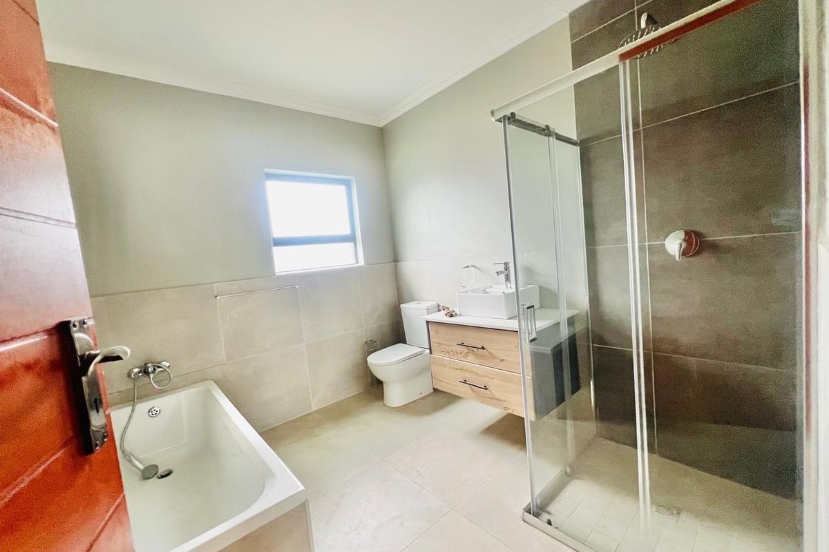 Modern bathroom featuring a glass-enclosed shower, a separate bathtub, a wall-mounted vanity with a vessel sink, and neutral floor-to-ceiling tiling.