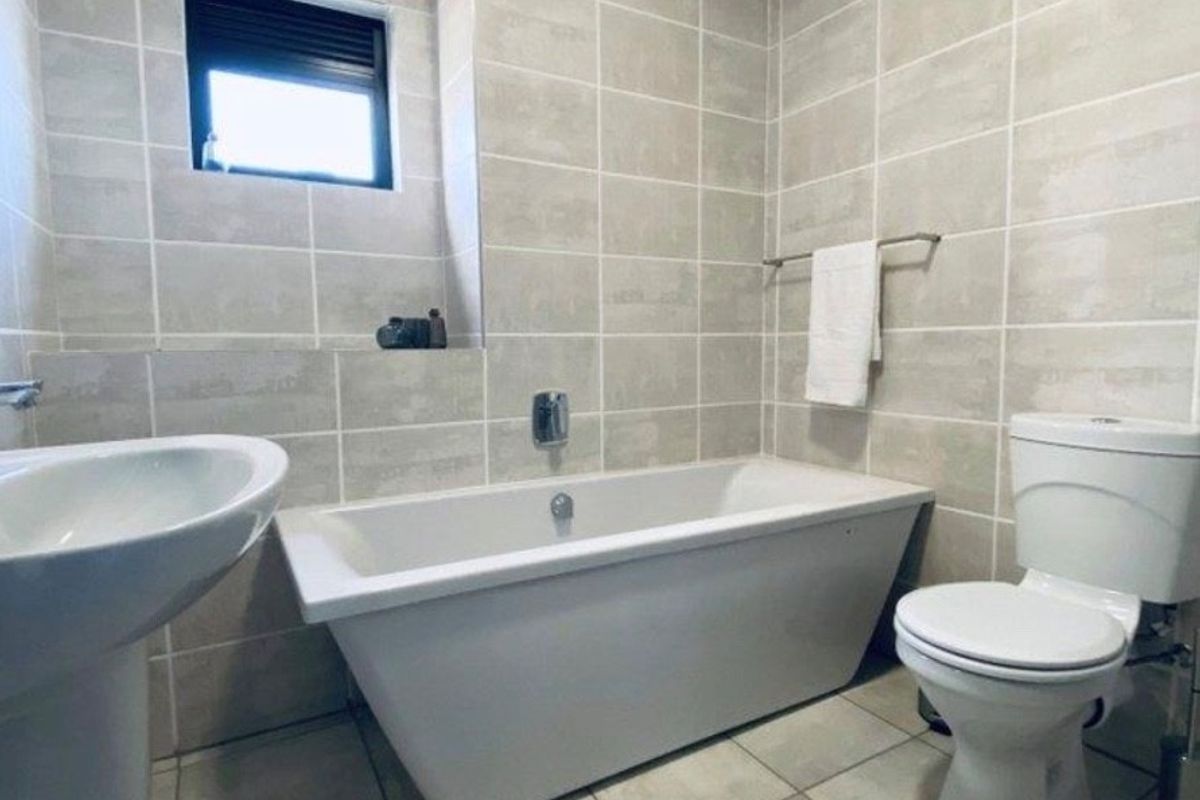 A modern bathroom featuring neutral wall and floor tiling, a white bathtub, a pedestal basin, and a toilet.