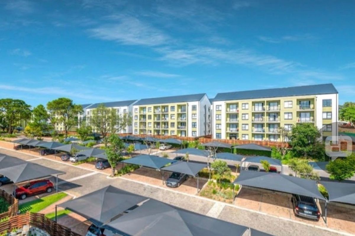 An aerial view of a modern apartment complex featuring multi-story residential buildings and extensive covered parking bays for residents.