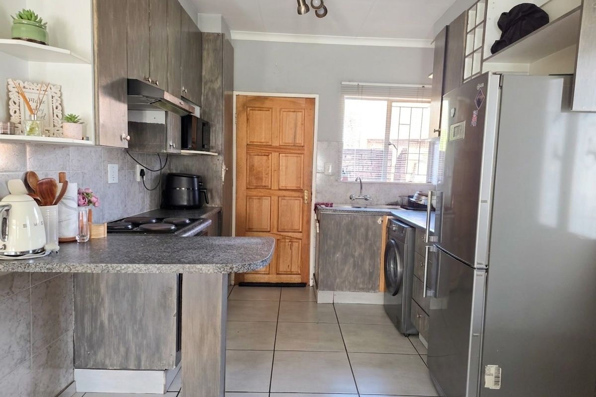 A functional kitchen featuring built-in cabinetry, a breakfast counter, tiled flooring, and integrated plumbing connections for laundry appliances.