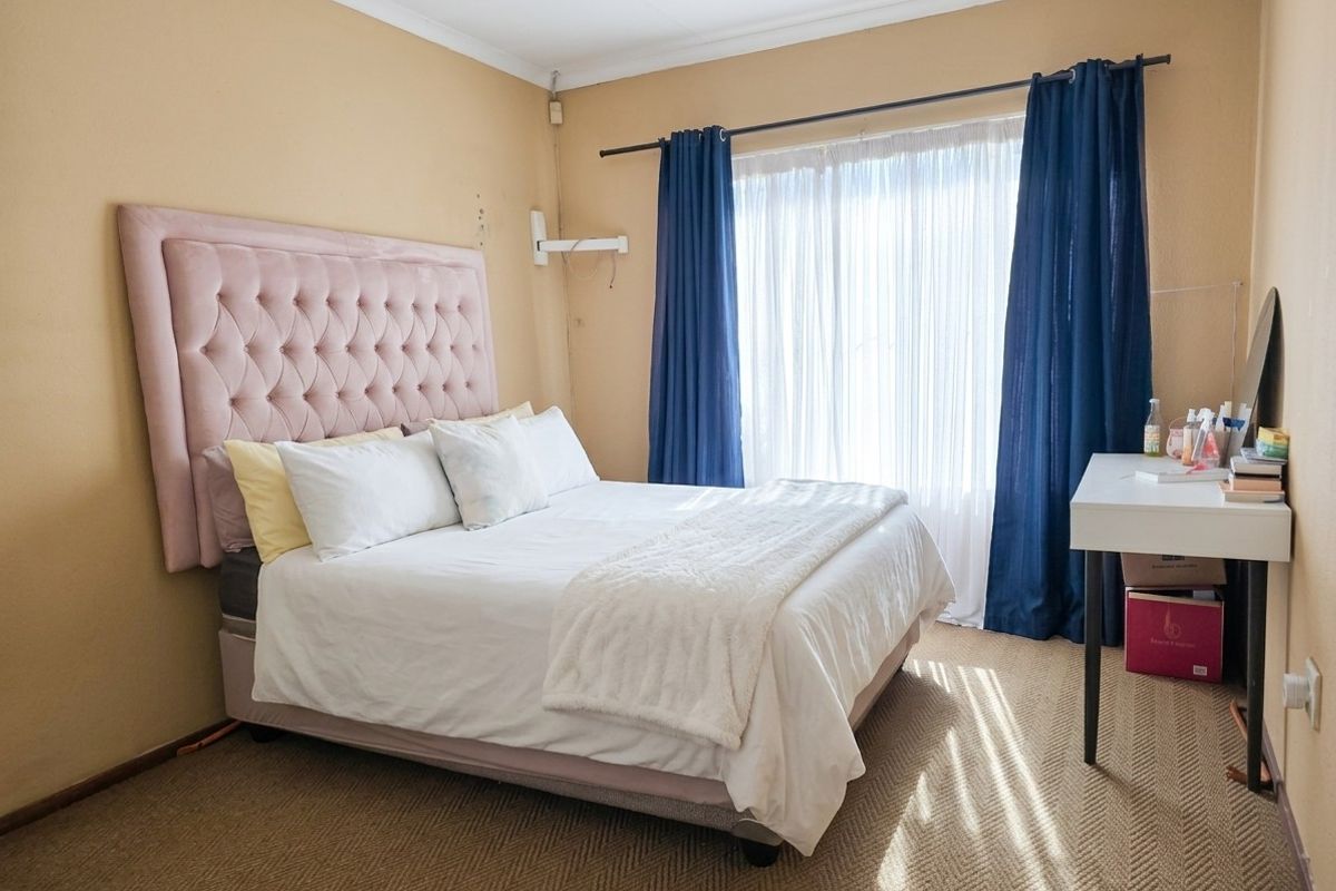 A bedroom featuring carpeted flooring, a large window with curtain rods, and neutral wall finishes.