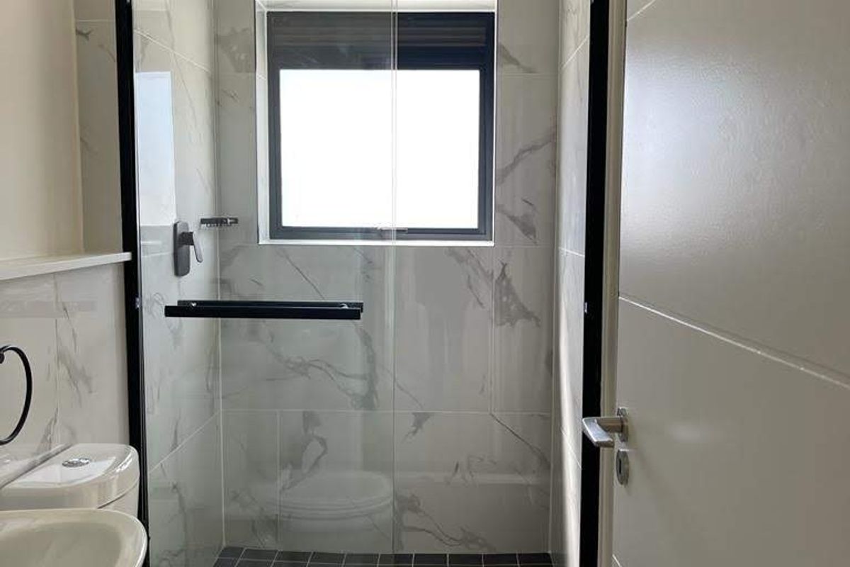 Modern bathroom featuring a walk-in shower with black frame, marble-look wall tiles, dark floor tiles, and a white pedestal basin.