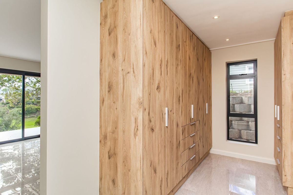 A modern bedroom featuring extensive floor-to-ceiling built-in wooden cabinetry, tiled flooring, and large windows providing natural light and garden views.