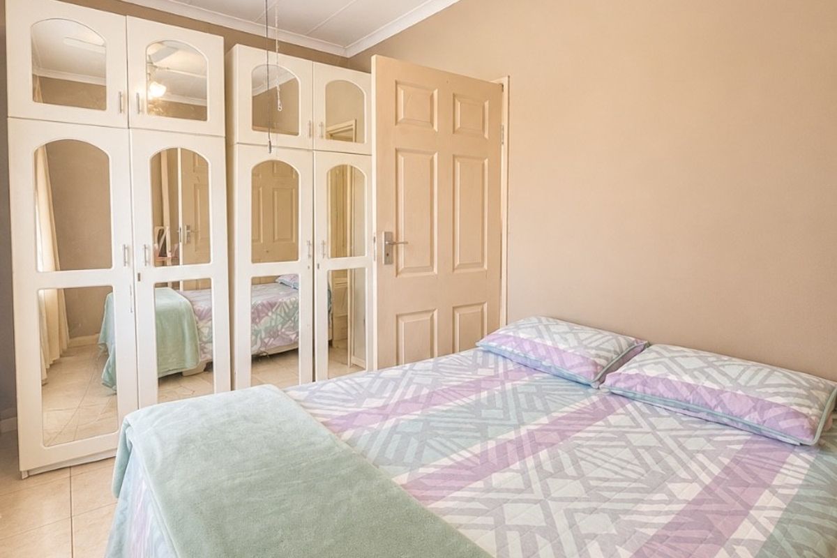 A bedroom featuring built-in mirrored wardrobes, tiled flooring, and a ceiling fan, offering a functional and neutral living space.