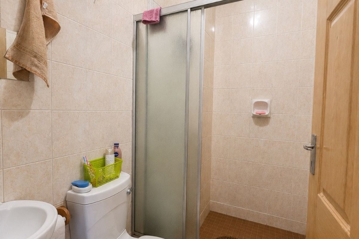 A compact bathroom featuring a tiled shower enclosure with sliding glass doors, a standard toilet, and a wall-mounted basin.