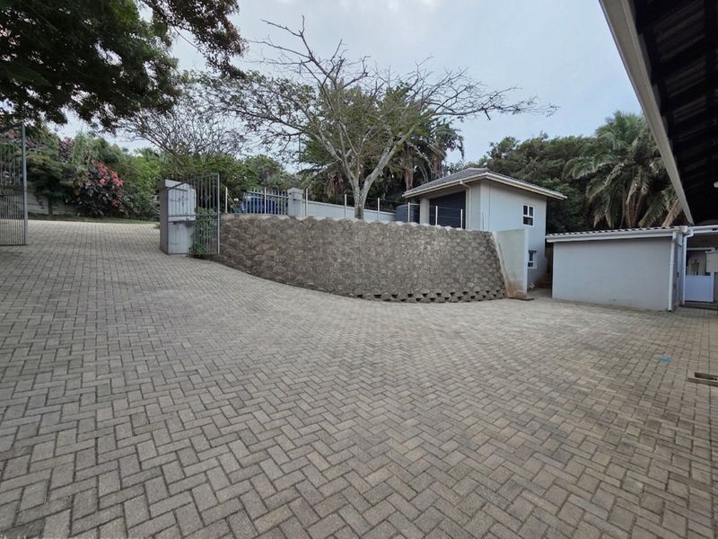 A spacious paved driveway leading to a garage, featuring a stone retaining wall and secure gated access.