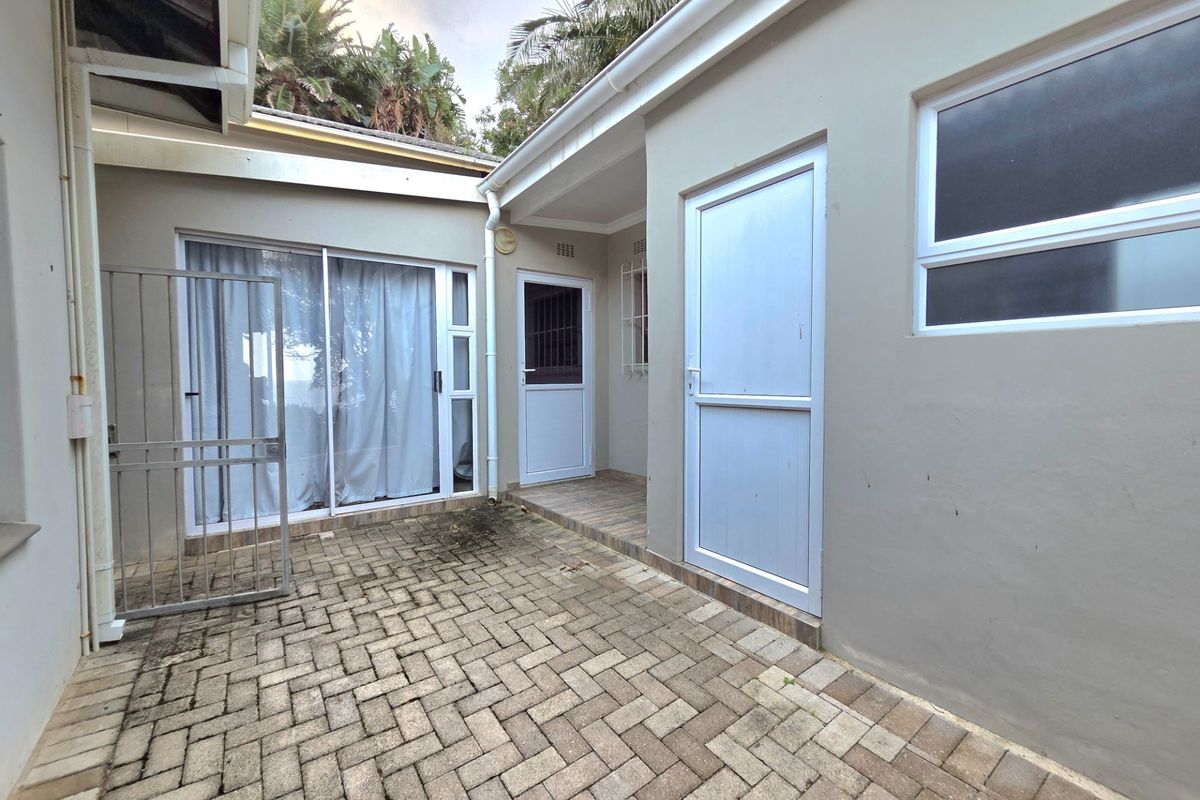 A paved rear courtyard area featuring a sliding glass door, security gate, and external access doors to the property.