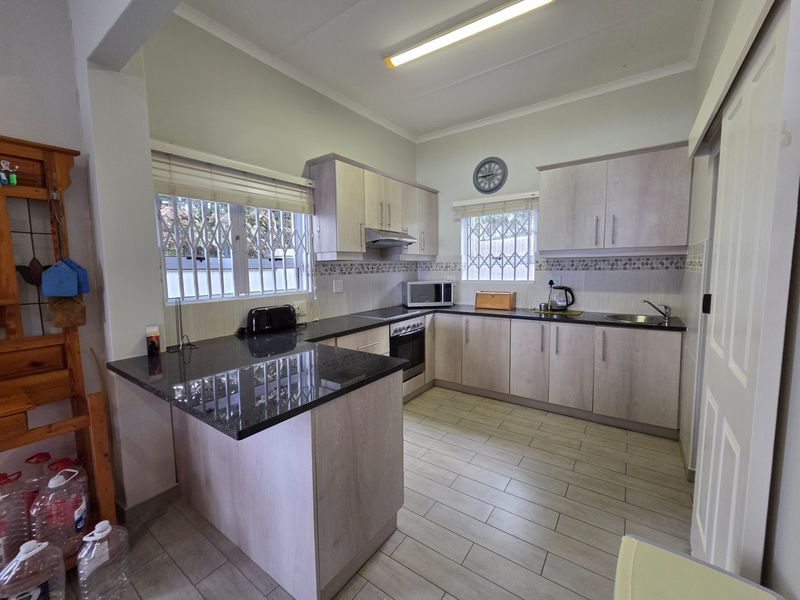 A functional kitchen featuring light wood-finish cabinetry, dark granite countertops, tiled flooring, and integrated stainless steel appliances with security bars on the windows.