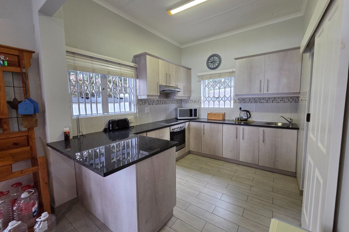 A functional kitchen featuring light wood-finish cabinetry, dark granite countertops, tiled flooring, and integrated stainless steel appliances with security bars on the windows.