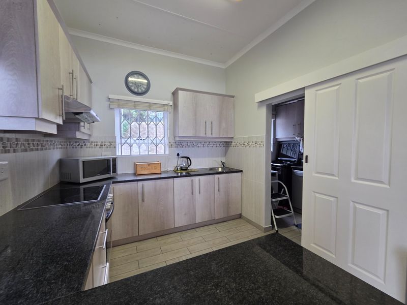 Modern kitchen featuring light wood cabinetry, dark granite countertops, electric hob, extractor fan, and a convenient sliding door leading to a scullery area.