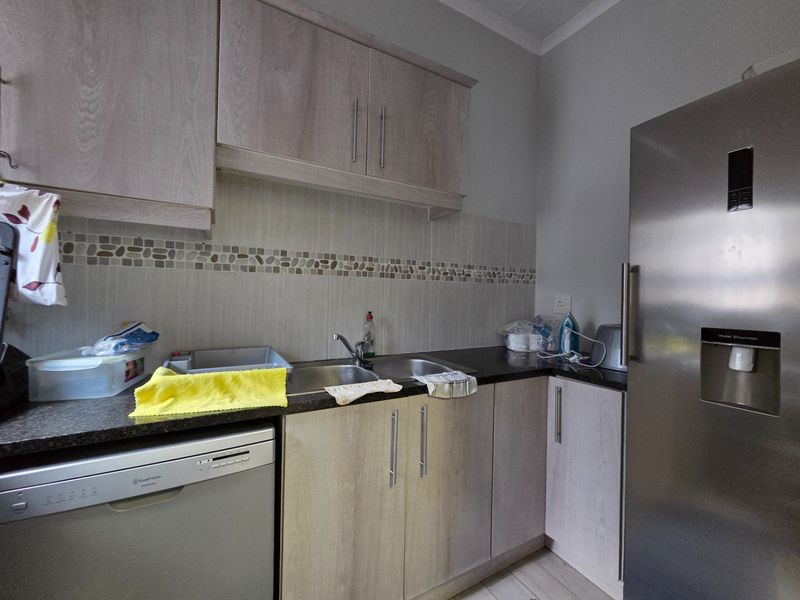 A functional kitchen featuring light wood-tone cabinetry, granite countertops, a double stainless steel sink, and a tiled backsplash with decorative accents.