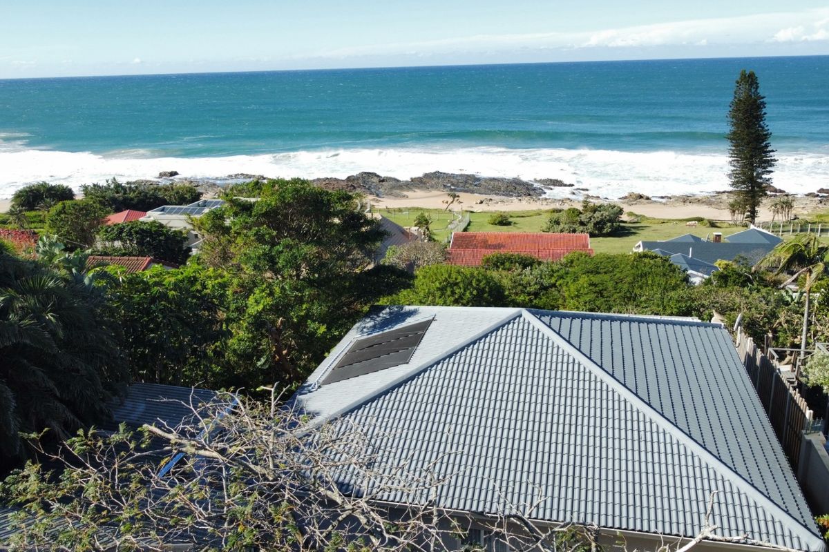 Aerial view of the property featuring a tiled roof with integrated solar panels, overlooking the coastal landscape and ocean.