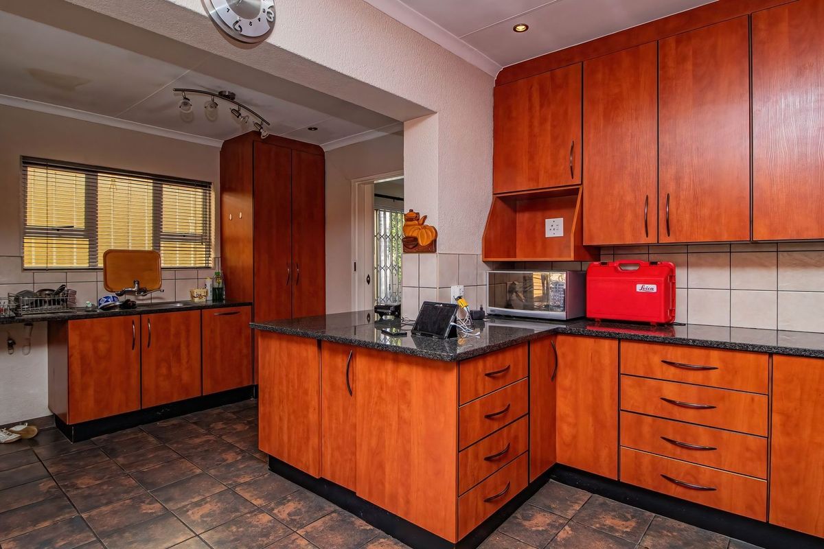 A functional kitchen featuring wood-veneer cabinetry, dark granite countertops, tiled splashbacks, and tiled flooring with an open-plan layout.
