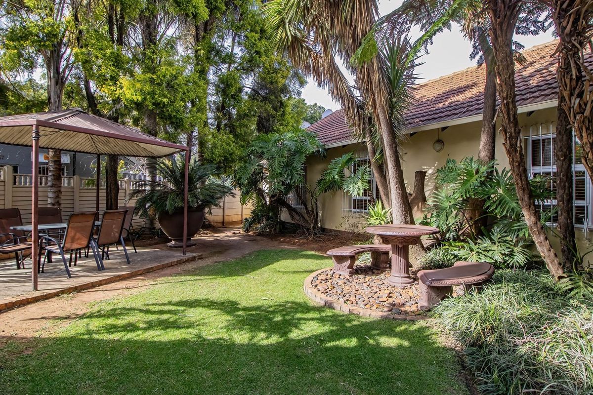 A private rear garden featuring a paved patio area with a gazebo, established trees, and a landscaped lawn with a stone-bordered seating area.