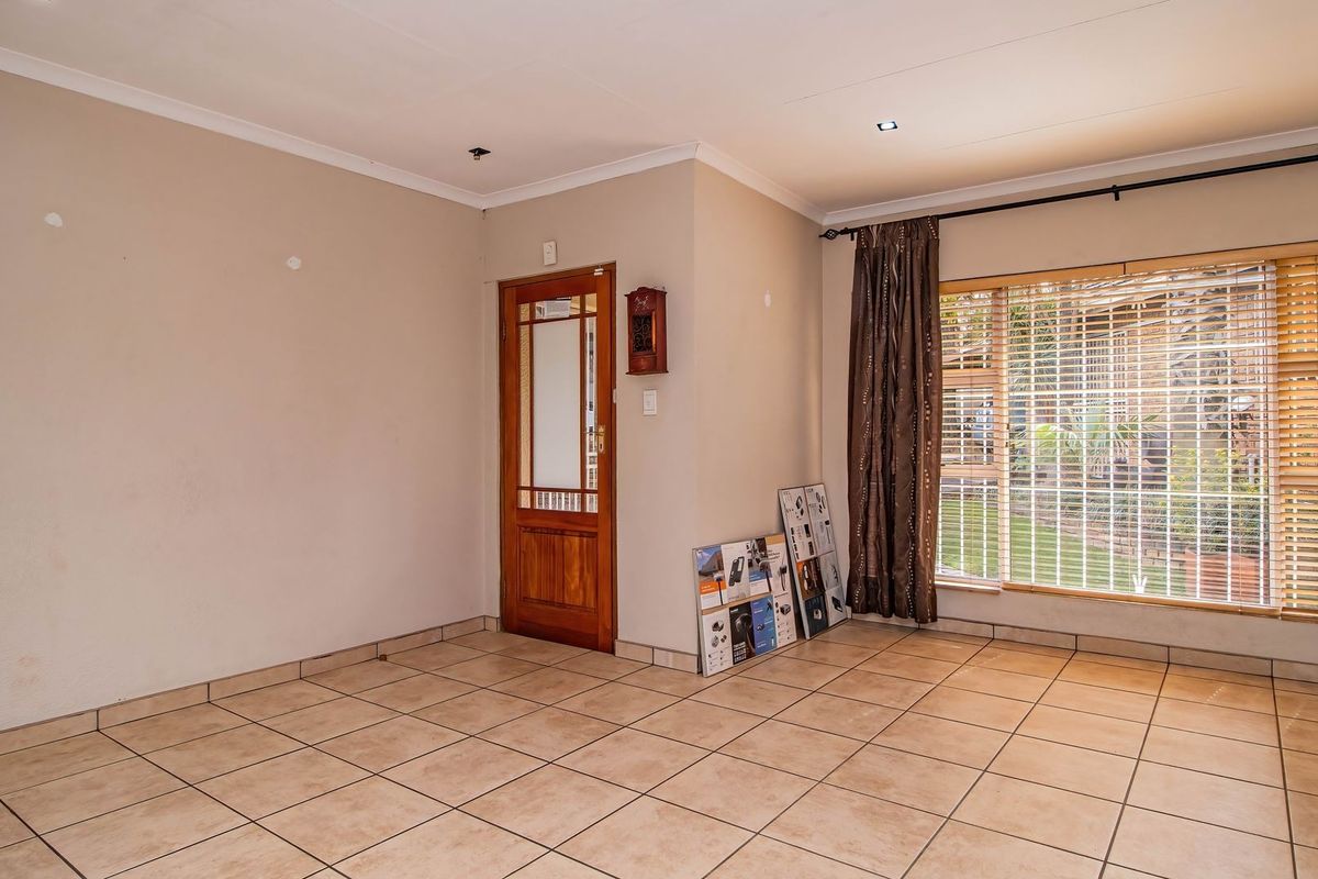 A spacious living area featuring neutral tiled flooring, a wooden entrance door, and large windows with security bars overlooking the garden.