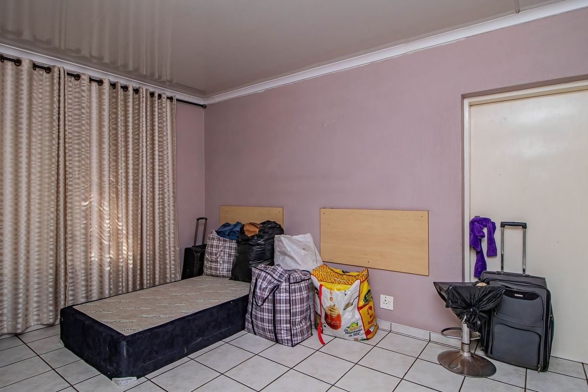 A bedroom featuring tiled flooring, a built-in headboard, and a standard door, currently used for storage.