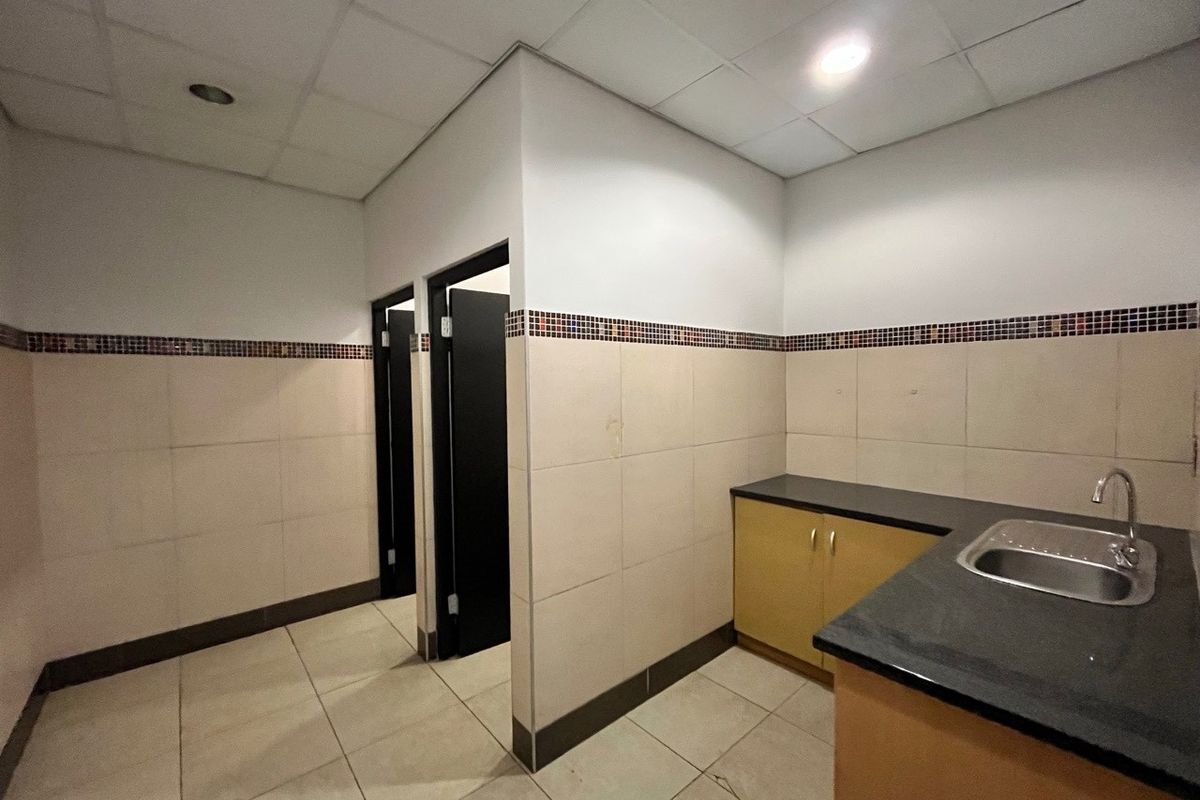 A functional office kitchenette area featuring tiled walls with mosaic accents, a built-in sink, and access to private restroom facilities.