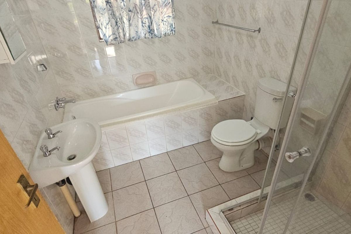 A functional bathroom featuring a built-in bathtub, separate glass-enclosed shower, pedestal basin, and toilet with tiled walls and flooring.