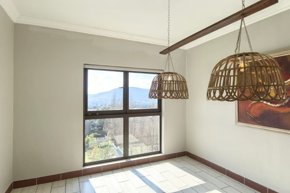 A bright, neutral-toned room featuring tiled flooring, crown molding, and a large window offering scenic mountain views.