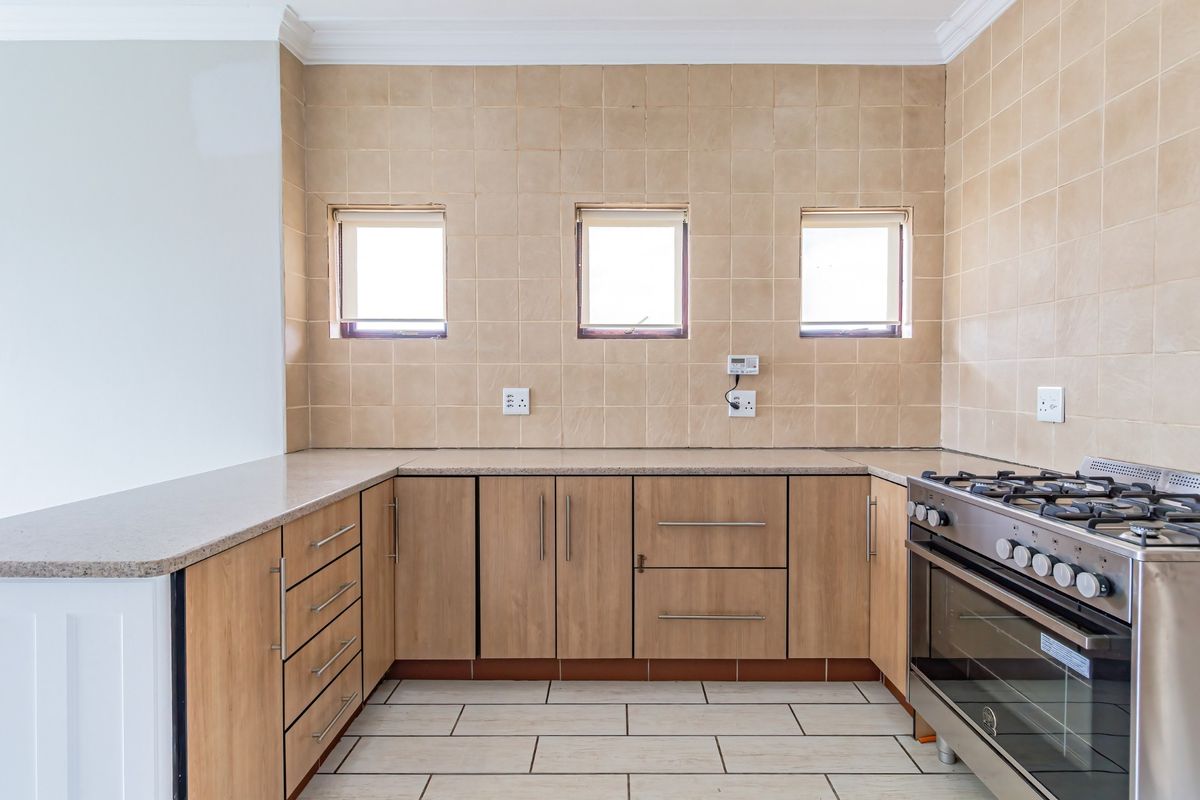 A functional kitchen featuring light wood cabinetry, stone-look countertops, tiled splashbacks, and a stainless steel gas stove.