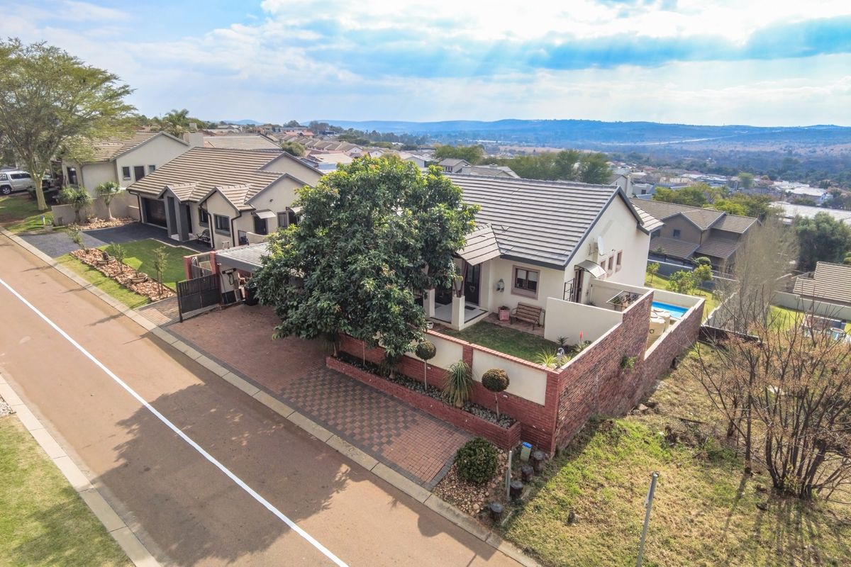 Aerial view of a residential property featuring a tiled roof, brick boundary wall, paved driveway, and a private swimming pool.