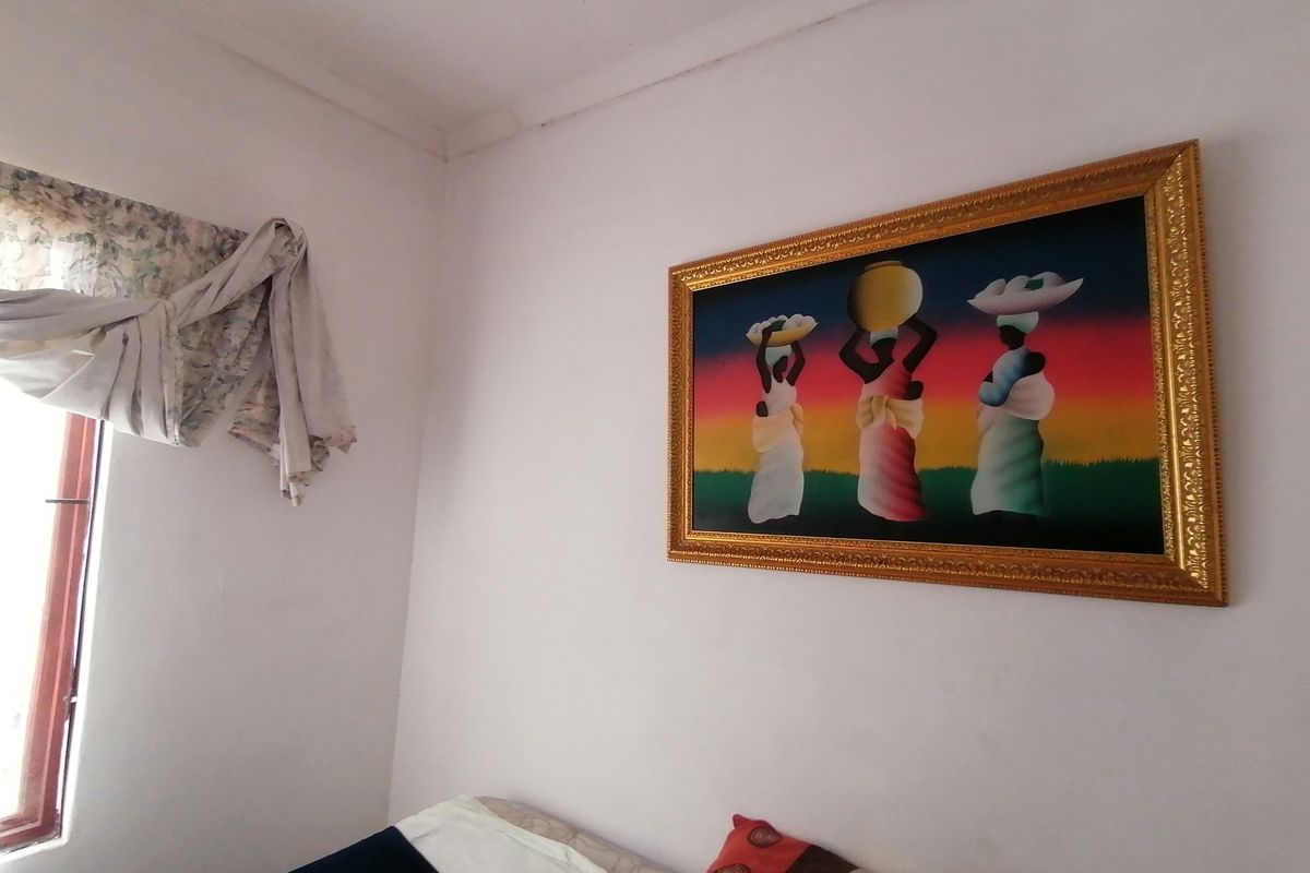 A bedroom featuring white walls, a window with a curtain, and a decorative framed artwork.