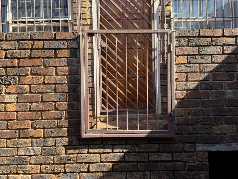 Exterior view of a cottage facade featuring face brick construction, security gates, and protective window bars.