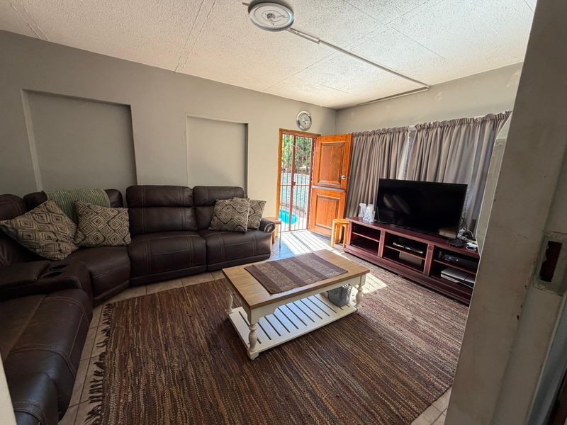 A living room featuring tiled flooring, recessed wall niches, and a wooden door providing direct access to the outdoor pool area.