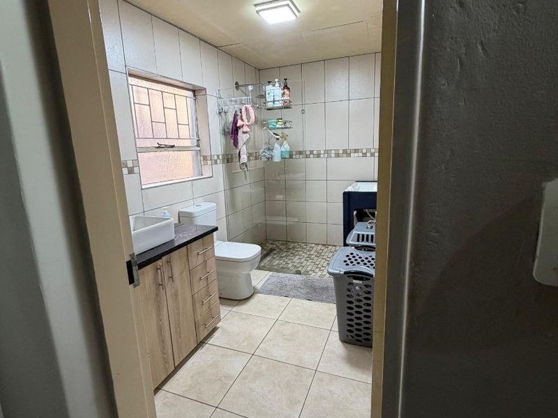 A functional bathroom featuring a vanity cabinet with a countertop basin, a toilet, and a walk-in shower area with tiled walls and flooring.