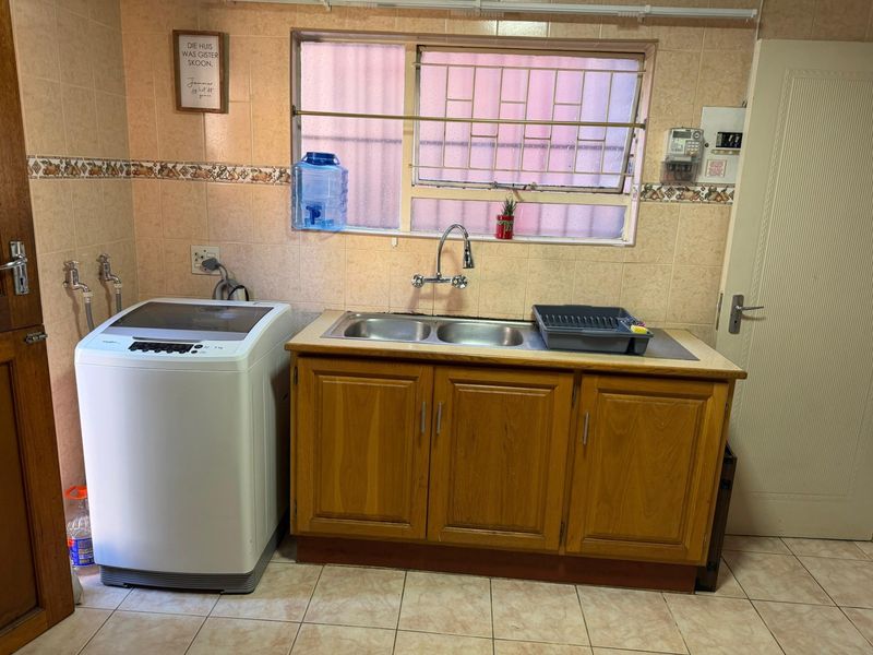 Functional laundry area featuring a double stainless steel sink, wooden cabinetry, and dedicated plumbing connections for a washing machine.
