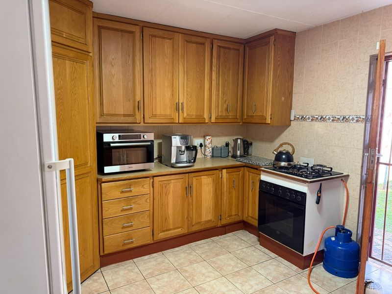 A functional kitchen featuring traditional oak cabinetry, tiled flooring, and a gas stove, offering a classic layout with direct access to the exterior.