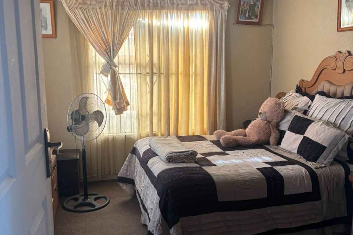A bedroom featuring dated ceiling tiles, carpet flooring, and a window with curtains, providing a functional sleeping space.
