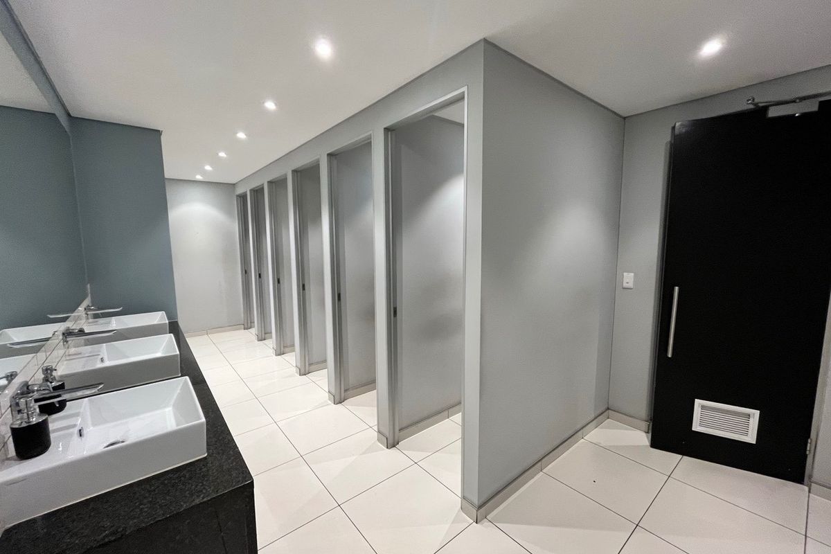Modern office restroom featuring multiple private stalls, sleek white vessel sinks on a dark granite vanity, and recessed ceiling lighting.
