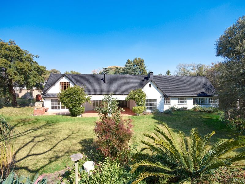 A well-maintained single-story residence featuring a dark tiled roof, white exterior walls, and a spacious rear garden with a covered patio area.