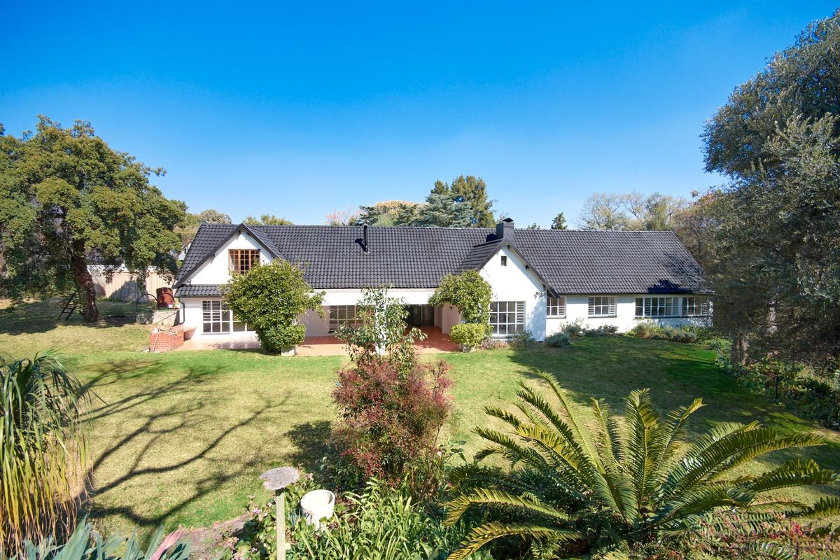 A well-maintained single-story residence featuring a dark tiled roof, white exterior walls, and a spacious rear garden with a covered patio area.