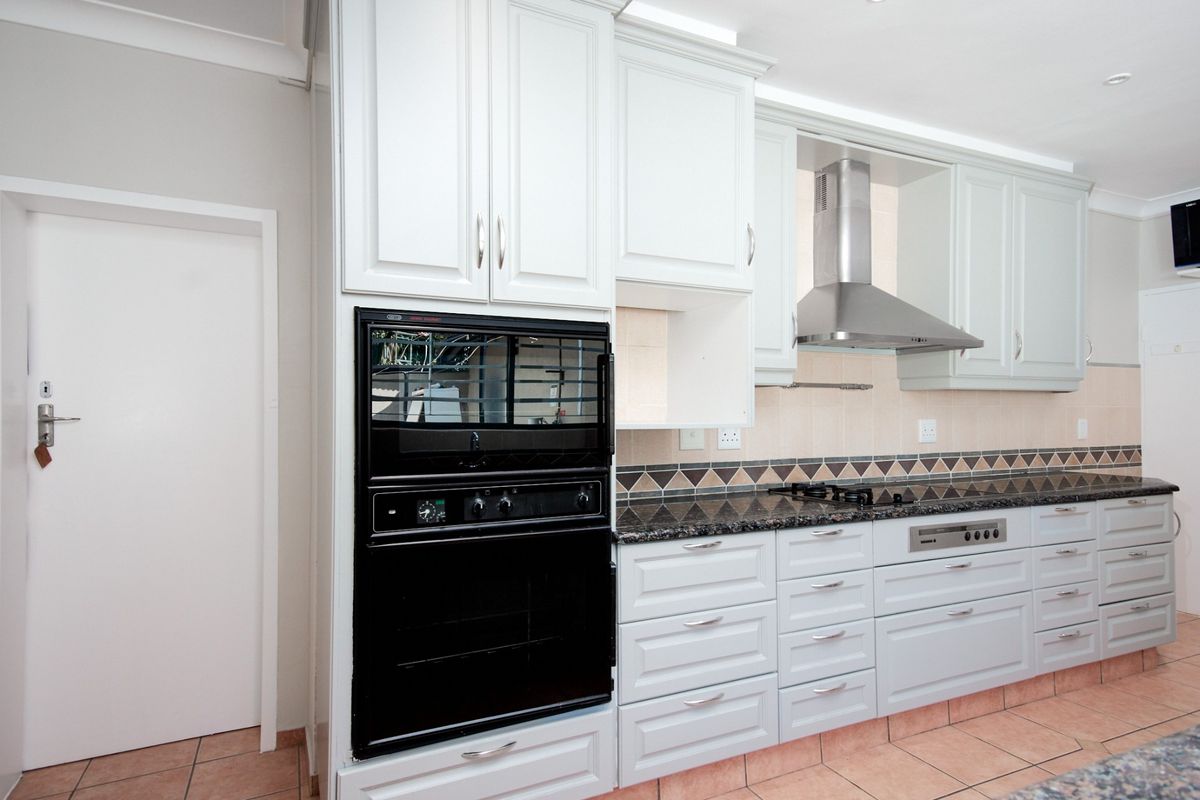 A clean, functional kitchen featuring white shaker-style cabinetry, granite countertops, a built-in oven, and a stainless steel extractor fan.