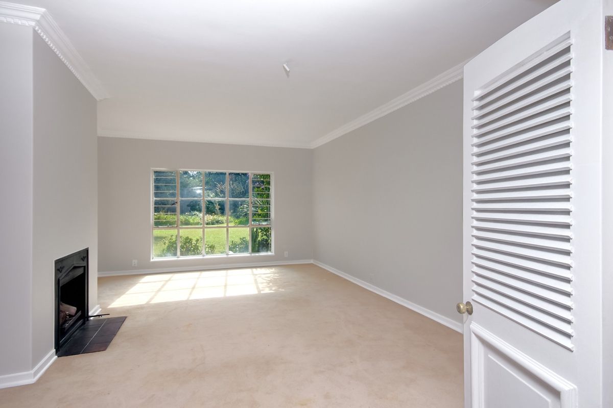 A bright, empty living room featuring a built-in fireplace, crown molding, and a large window overlooking the garden.