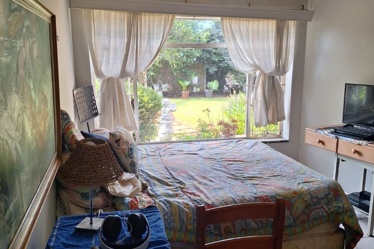 A bedroom featuring tiled flooring, a large window overlooking the garden, and a classic chandelier fixture.