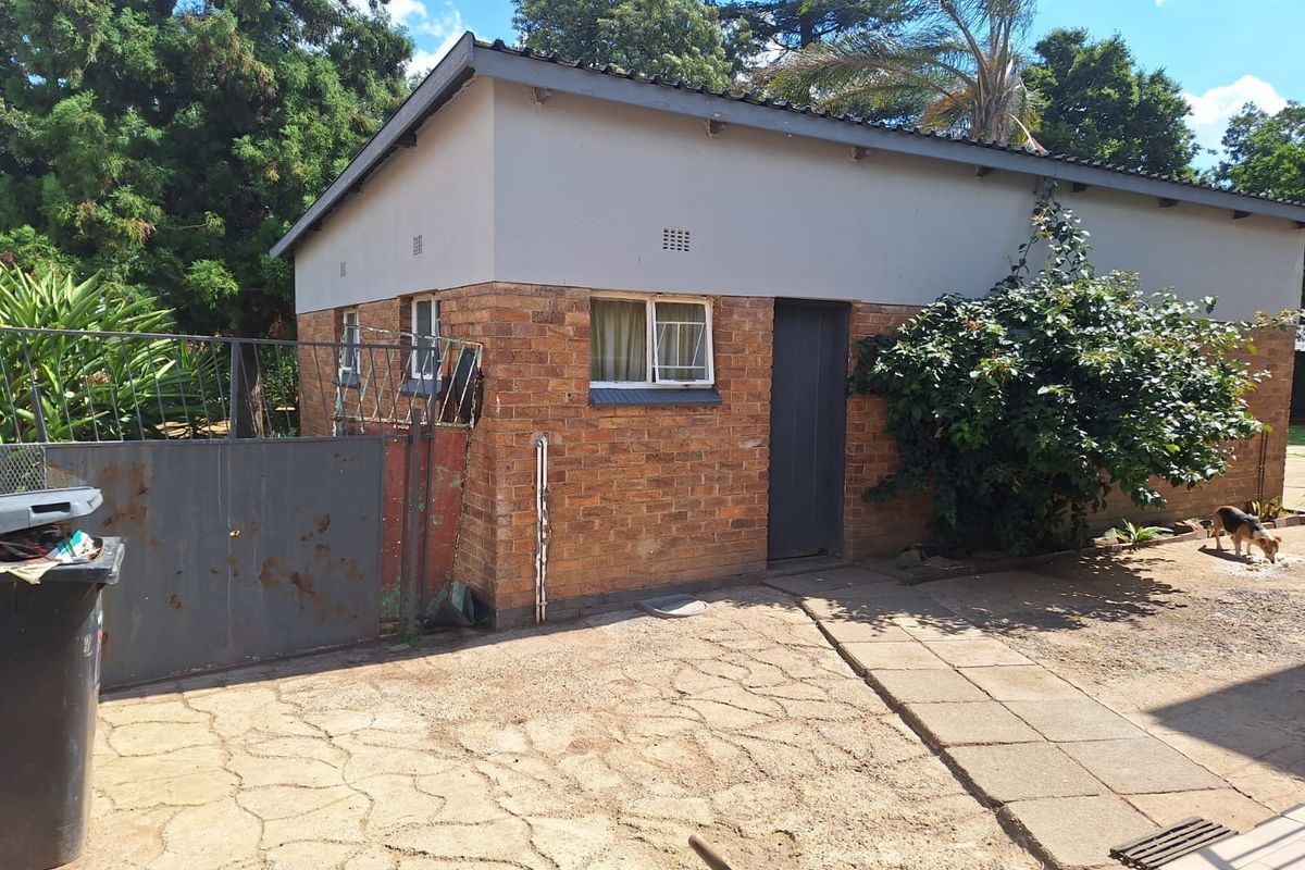 Exterior view of a detached brick outbuilding featuring a metal gate, paved walkway, and simple window and door access.