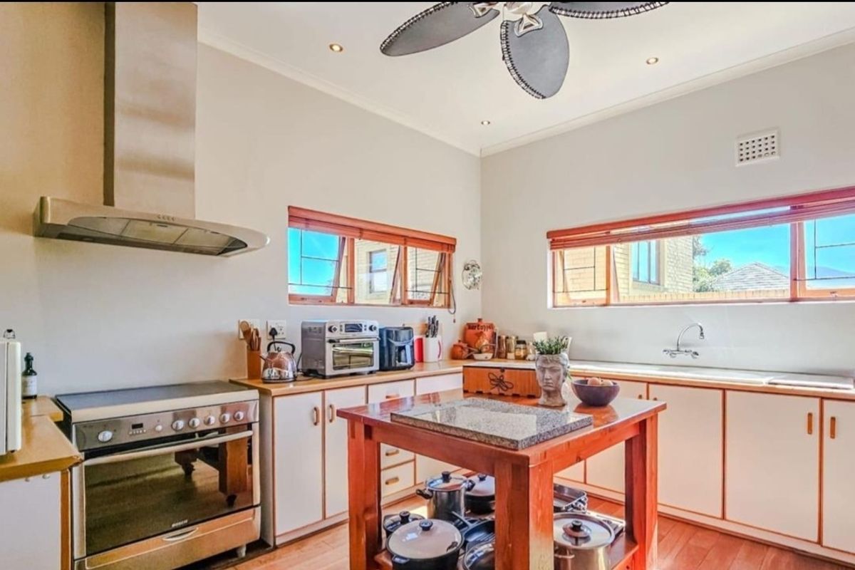 A functional kitchen featuring white cabinetry, wooden countertops, a stainless steel extractor fan, a freestanding oven, and a central wooden island.