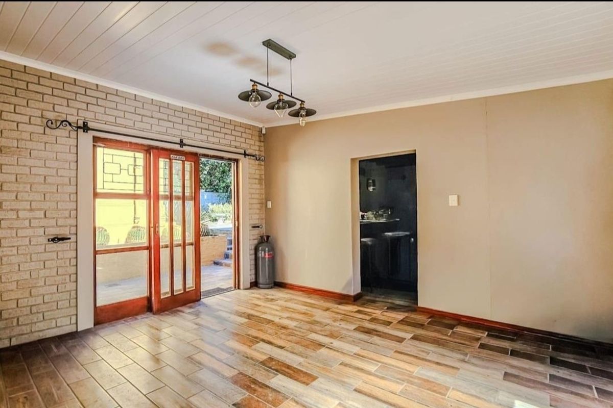 A spacious living area featuring exposed brickwork, wood-look tiled flooring, and sliding glass doors providing direct access to the outdoor patio.