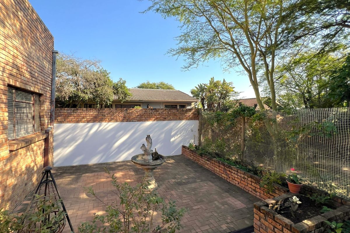 A private rear courtyard featuring brick paving, a perimeter brick wall, and a raised garden bed, offering a quiet outdoor space.