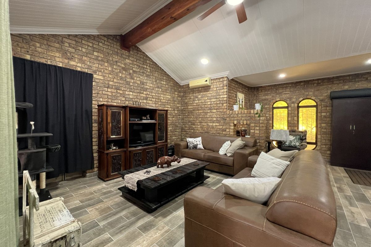 Spacious living room featuring exposed brick walls, vaulted ceilings with timber beams, tiled flooring, and arched windows.